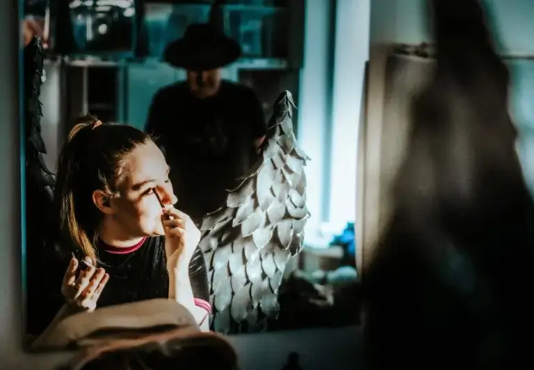 Artisti meikkaa peilin edessä. Taustalla väijyy tumma hahmo.