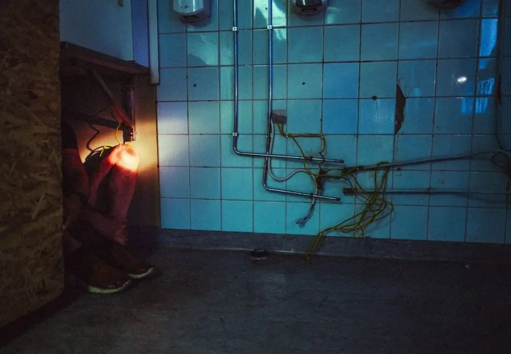 Piileskelevän miehen jalat pilkottavat hämärässä pöydän alta.